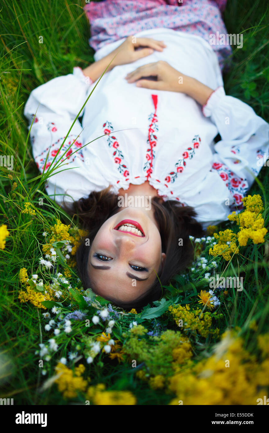 Giovane bella ragazza sorridente in ucraino costume con una corona di fiori alla sua testa in un prato Foto Stock