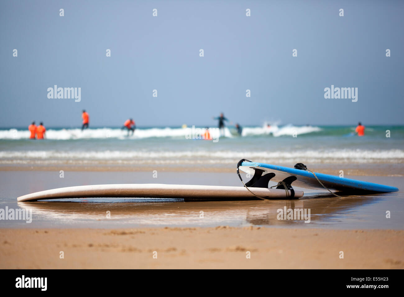 Gruppo di persone aventi lezioni di surf tra le onde su una spiaggia di sabbia in Spagna e tavole da surf in primo piano cielo blu in background Foto Stock