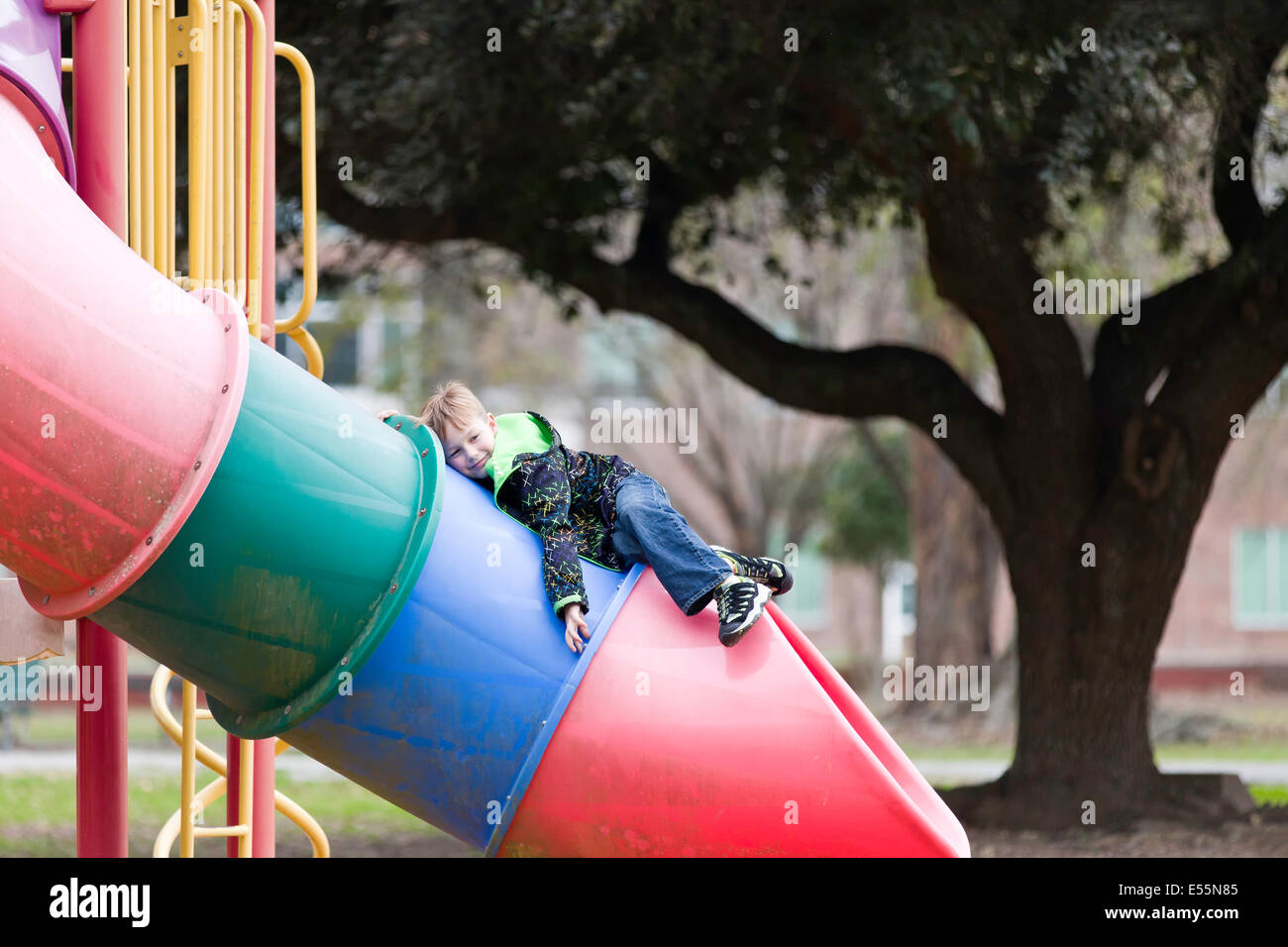 Un giovane ragazzo si appoggia sulla cima di un tubo colorato scorrere in corrispondenza di un parco giochi in Louisiana. Foto Stock