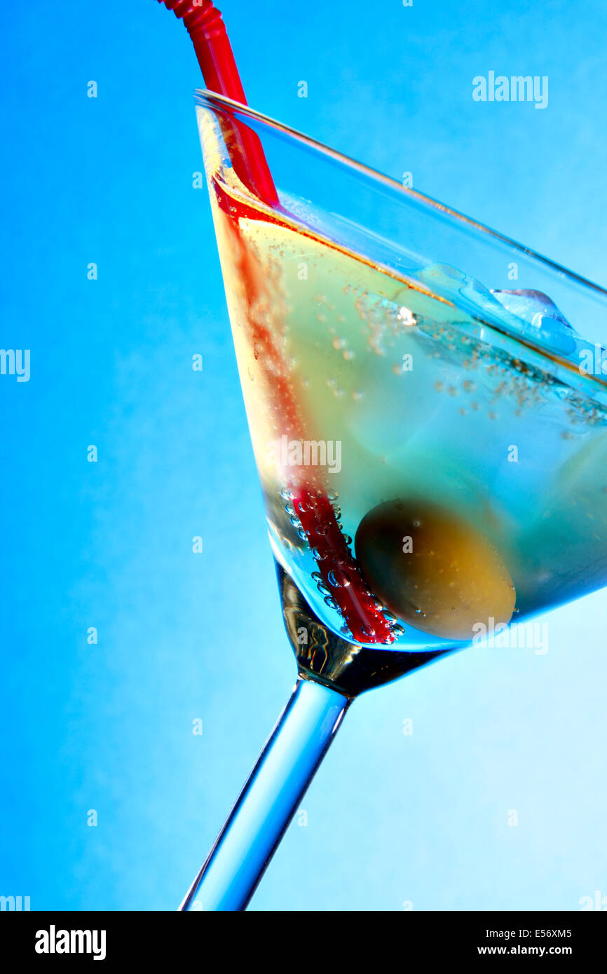 Bicchiere da cocktail con olive e paglia di rosso su sfondo blu Foto Stock