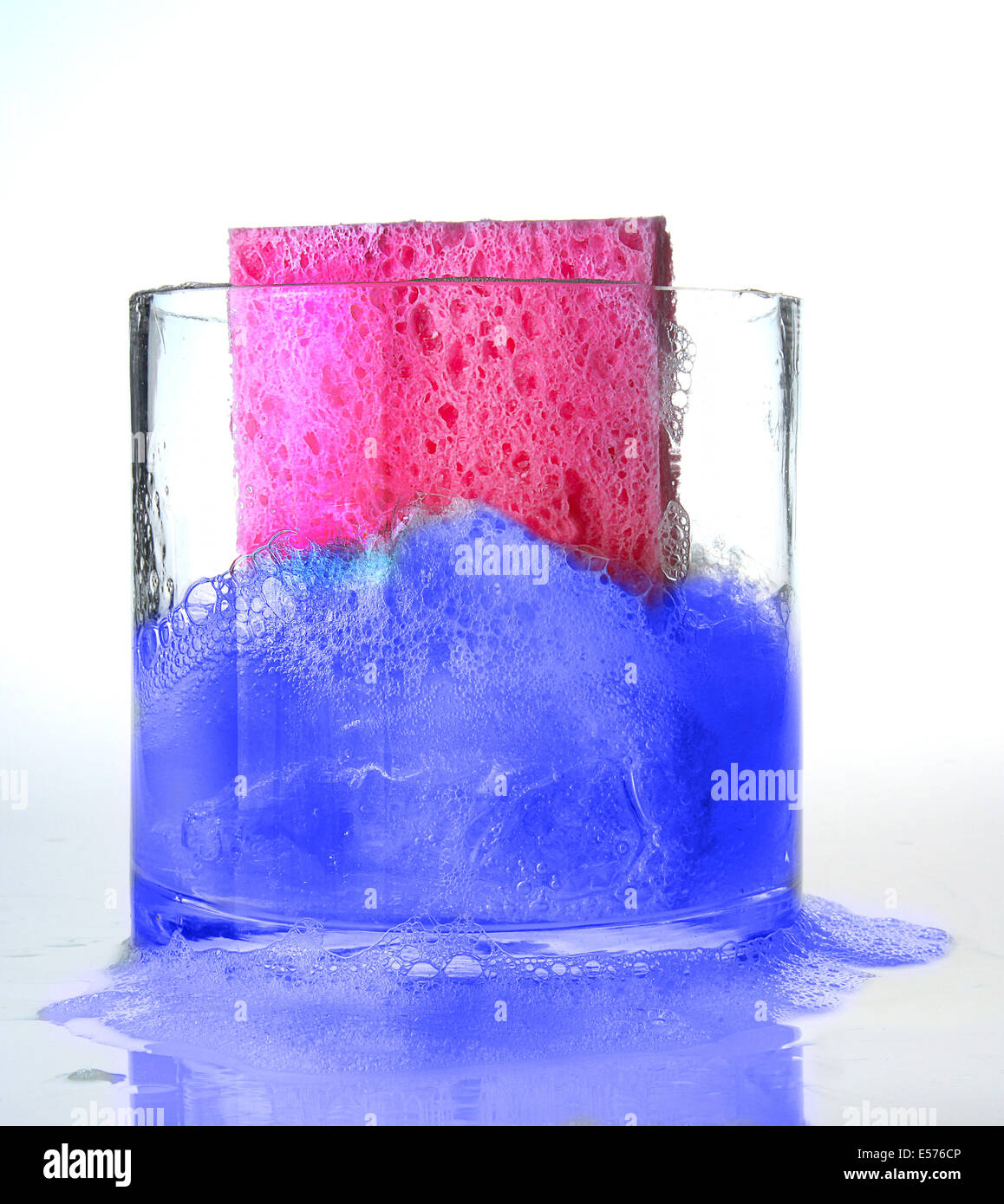 Spugna rosa cadere in blu con acqua saponata nel contenitore in vetro Foto Stock