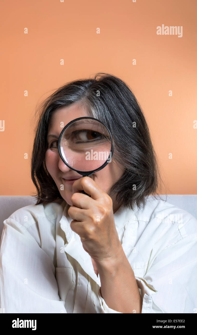 Immagine divertente di una donna adulta con una lente di ingrandimento, un occhio è ingrandita. Foto Stock