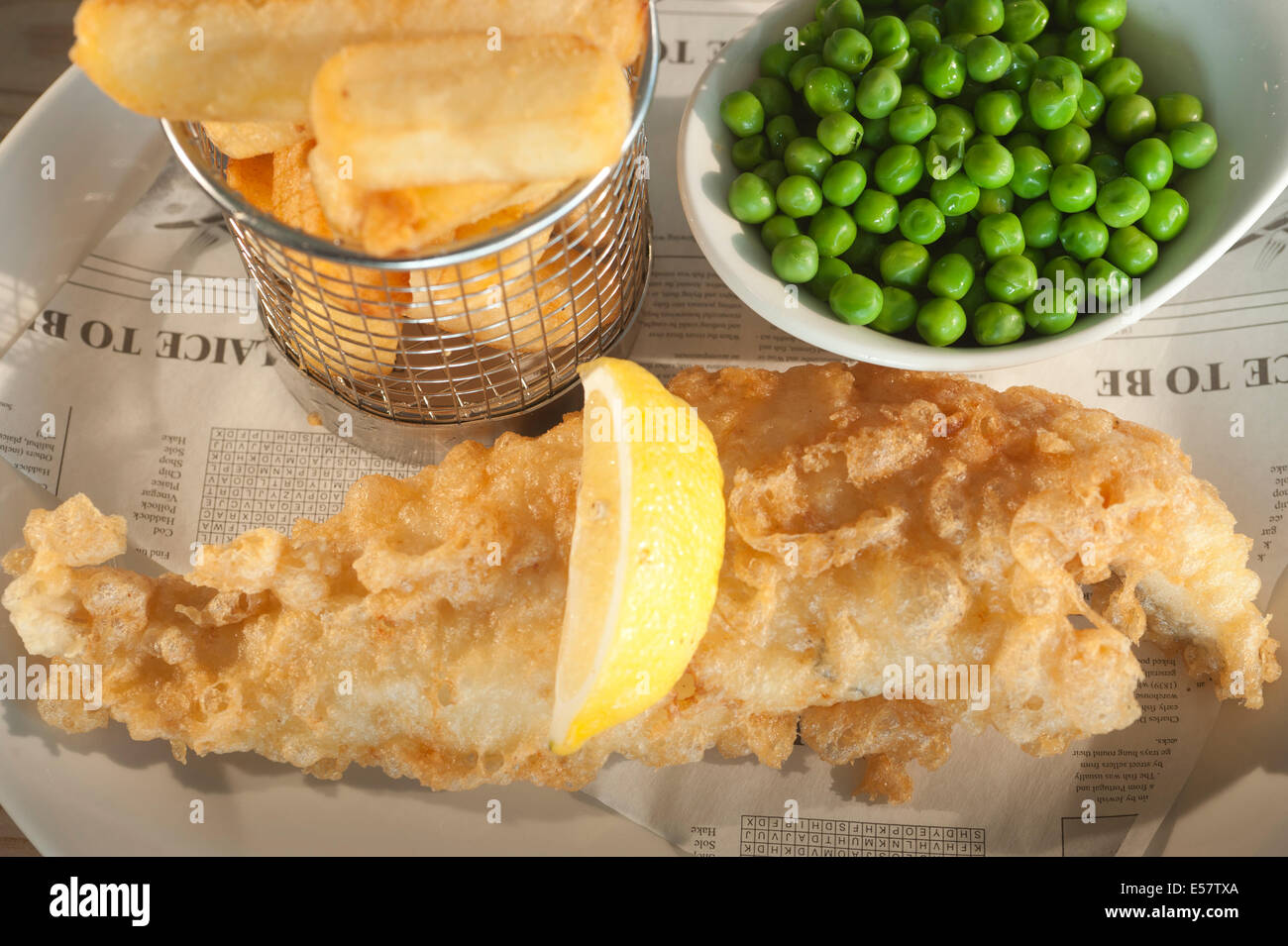 Fritti di pesce (Eglefino) e i chip con giardino di piselli e un segmento di limone su un finto stile giornale Carta di rinforzo. Foto Stock