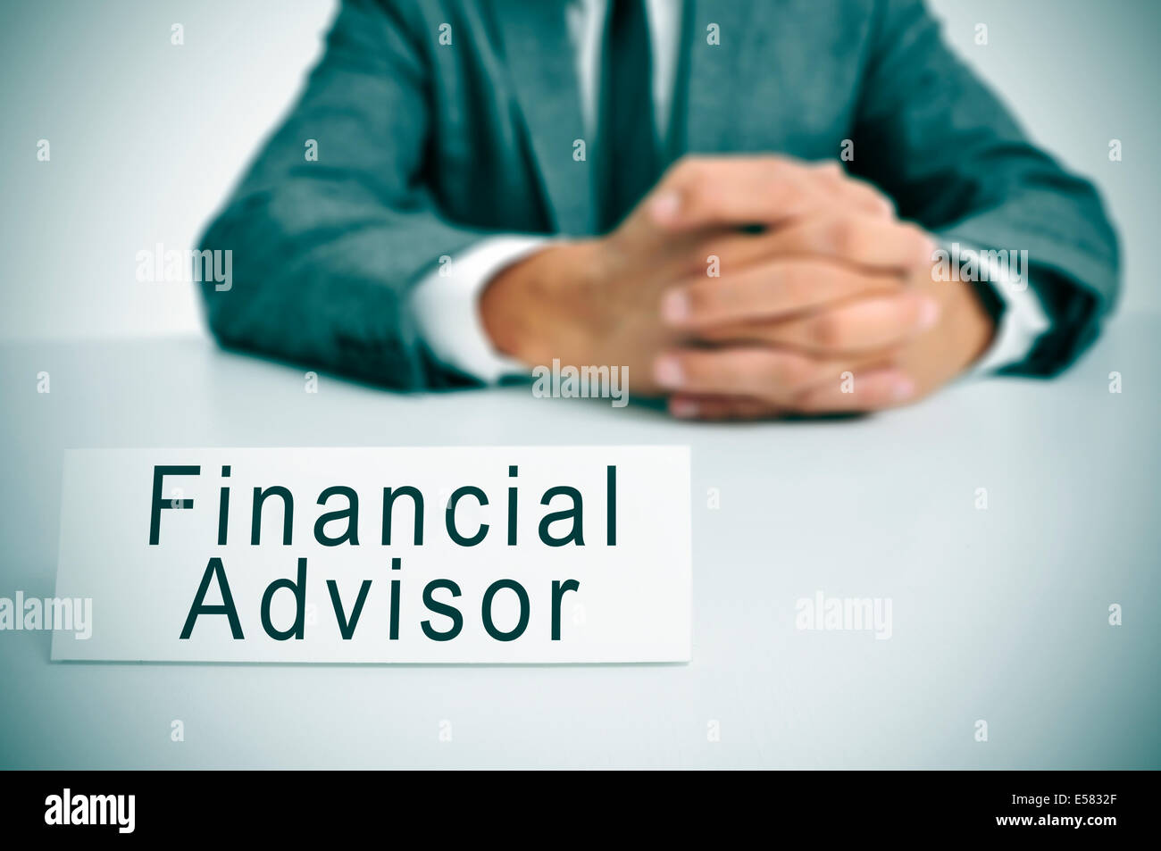 Un uomo che indossa una tuta seduti ad una scrivania con un cartello davanti a lui con il testo di advisor finanziario scritto in esso Foto Stock