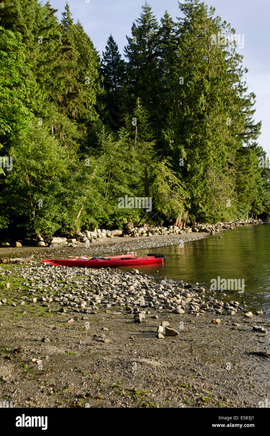 Due red kayak seduto sulla spiaggia rocciosa dall'acqua e foresta di Belcarra parco regionale più in Vancouver, BC, Canada Foto Stock