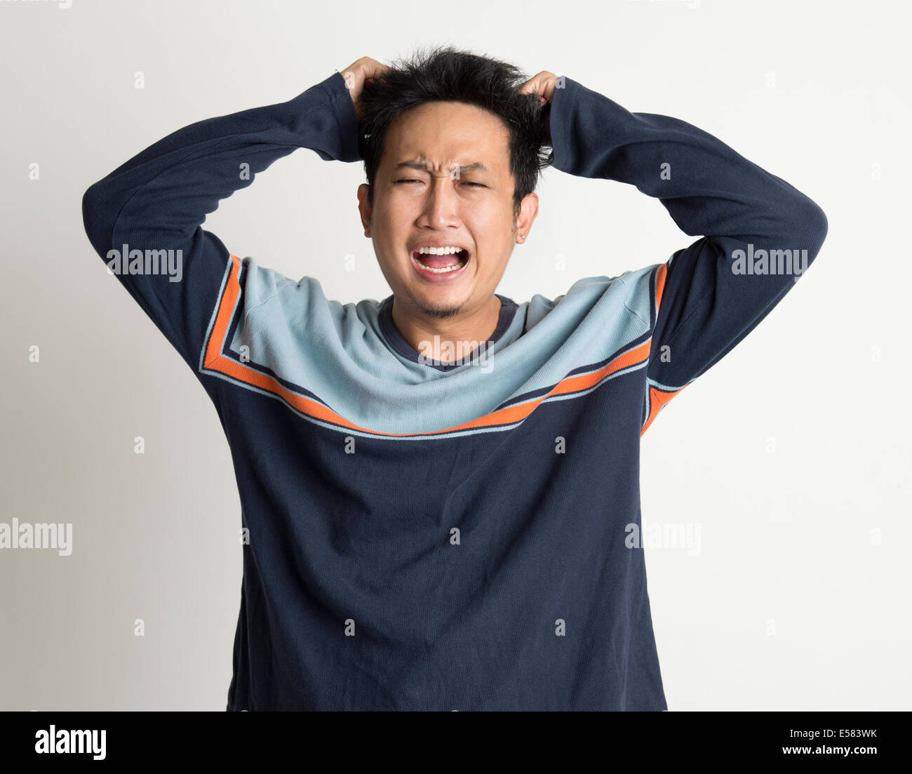 Ritratto di Mad Uomo asiatico tirando i suoi capelli su sfondo semplice Foto Stock