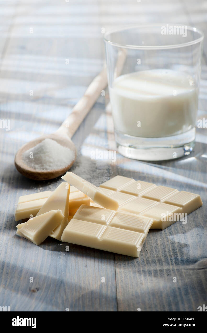 Il cioccolato bianco bar con lo zucchero e il bicchiere di latte, sul tavolo di legno illuminata dal sole Foto Stock Il cioccolato bianco bar con lo zucchero e il bicchiere di latte, sul tavolo di legno illuminata dal sole Foto Stock