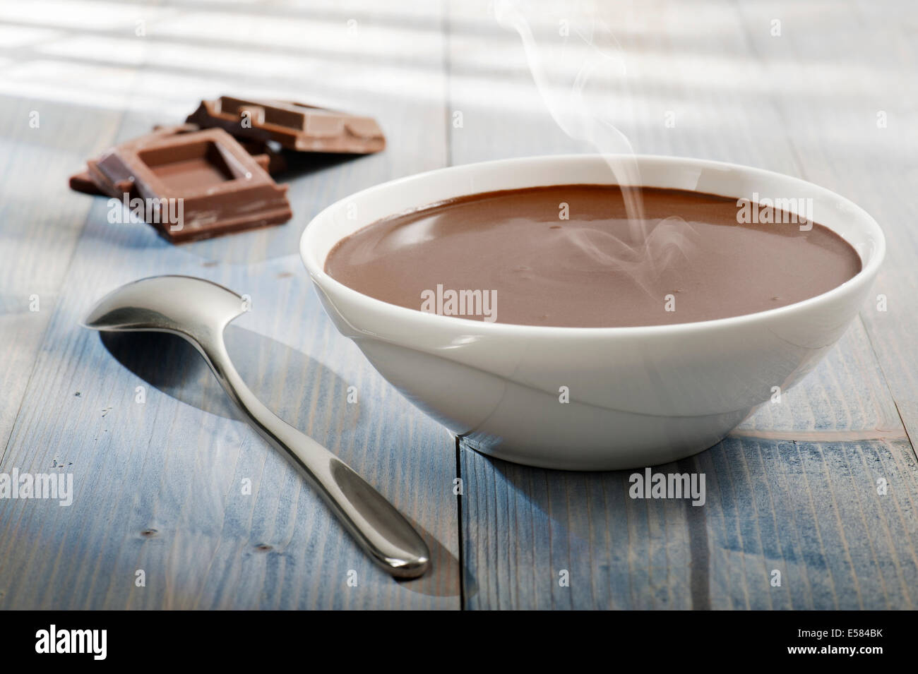 Tazza di caldo cioccolato fuso con cucchiaio e blocchi di cioccolato su un tavolo di legno con la luce solare Foto Stock Tazza di caldo cioccolato fuso con cucchiaio e blocchi di cioccolato su un tavolo di legno con la luce solare Foto Stock