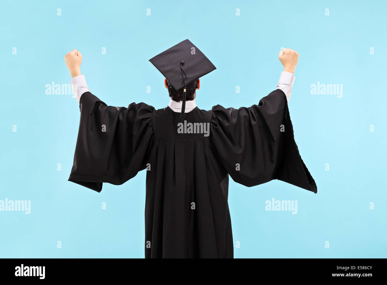 Overjoyed studente laureato con pugni in rilievo su sfondo blu, vista posteriore Foto Stock