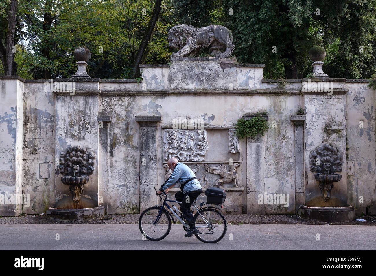 L'uomo corse la sua bici passato una rustica Fontana nella Villa Borghese, Roma, Italia Foto Stock