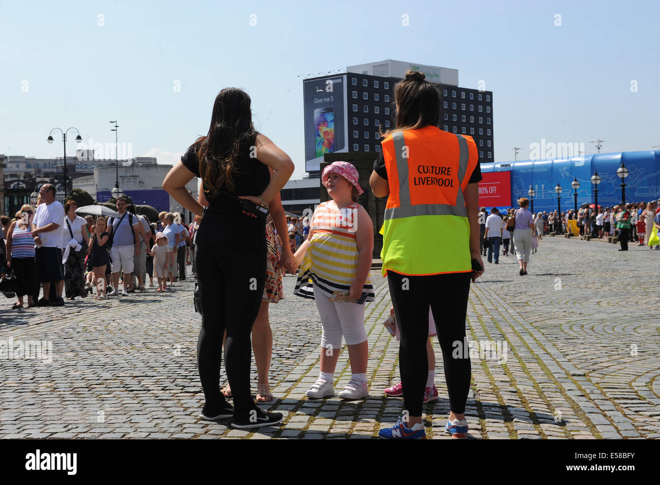 Liverpool, Regno Unito. Il 23 luglio 2014. Hugh folla coda fuori per visitare St George's Hall per vedere la nonna gigante, come lei ottiene il suo sonno prima del suo viaggio intorno a Liverpool. Quest'anno la storia dei giganti si concentra sulla WW1 centenario e 'Memories di agosto 1914'. La mostra oltre il prossimo fine settimana è da francese di teatro di strada esperti Royal De Luxe. Una cultura Liverpool steward aiuta i visitatori a St George's Hall Credito: David Colbran/Alamy Live News Foto Stock