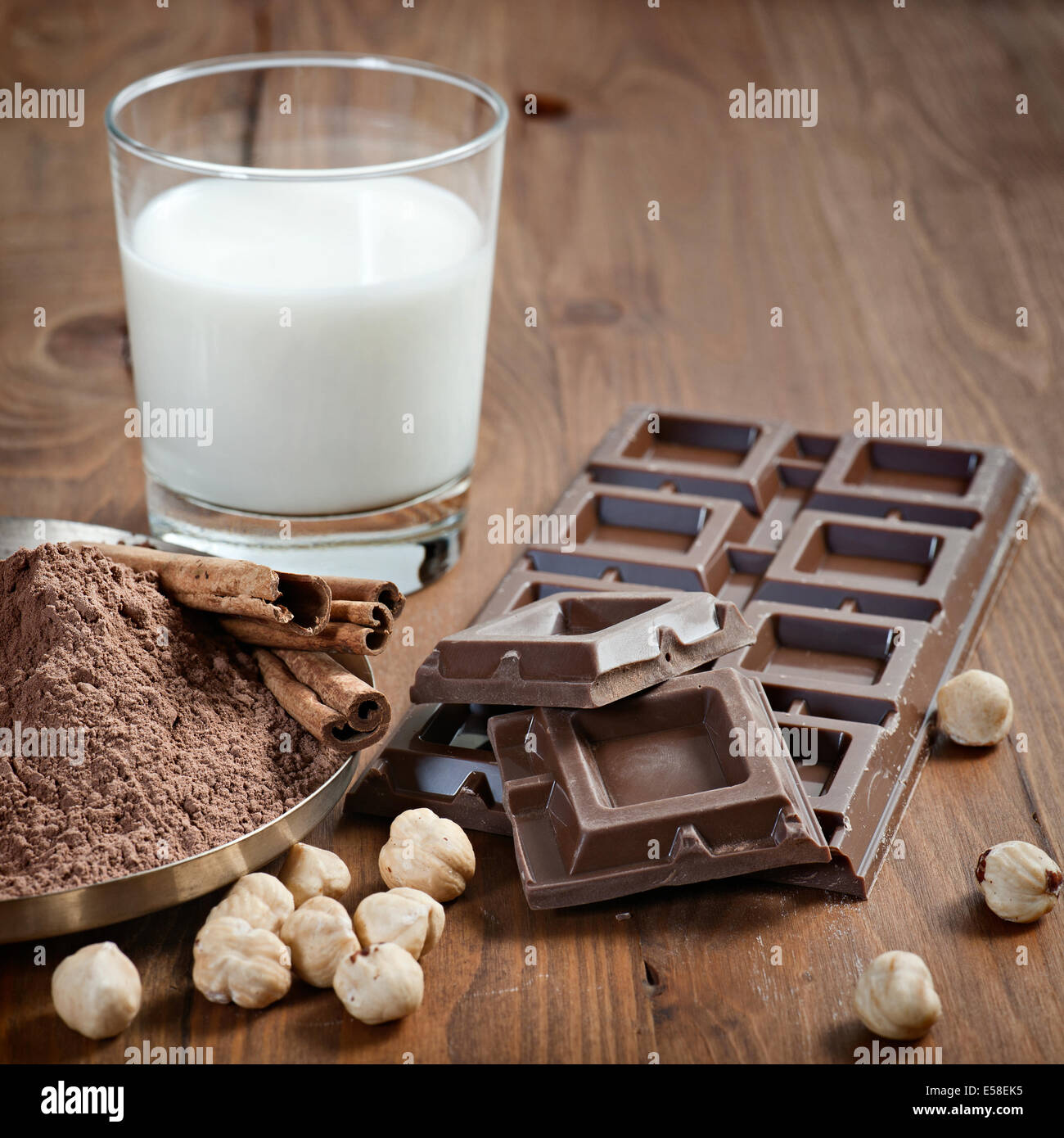 Barra di cioccolato con polvere di cacao, cannella, frutta in guscio e latte su uno sfondo di legno Foto Stock Barra di cioccolato con polvere di cacao, cannella, frutta in guscio e latte su uno sfondo di legno Foto Stock