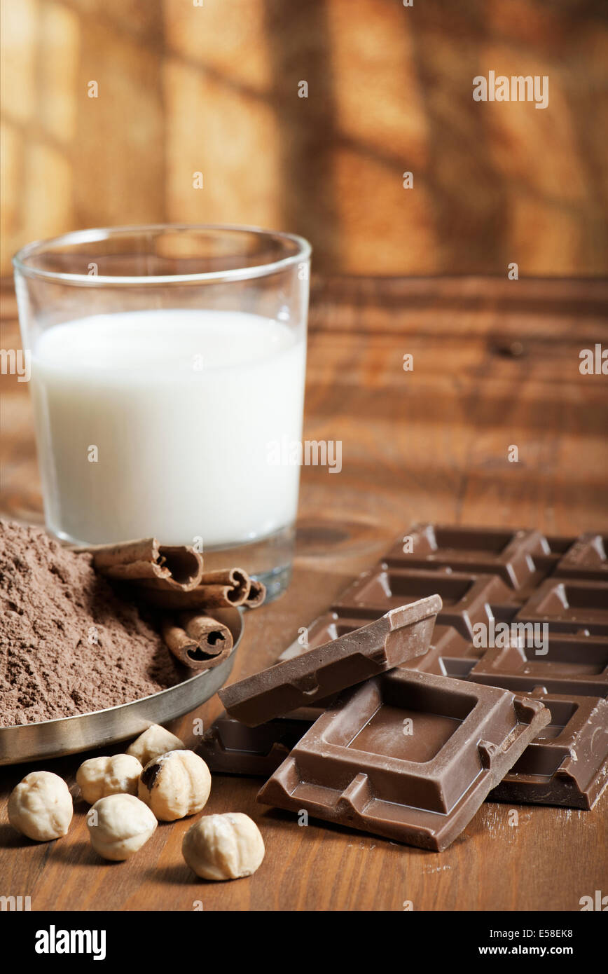 Barra di cioccolato con polvere di cacao, cannella, frutta in guscio e latte su uno sfondo di legno Foto Stock Barra di cioccolato con polvere di cacao, cannella, frutta in guscio e latte su uno sfondo di legno Foto Stock