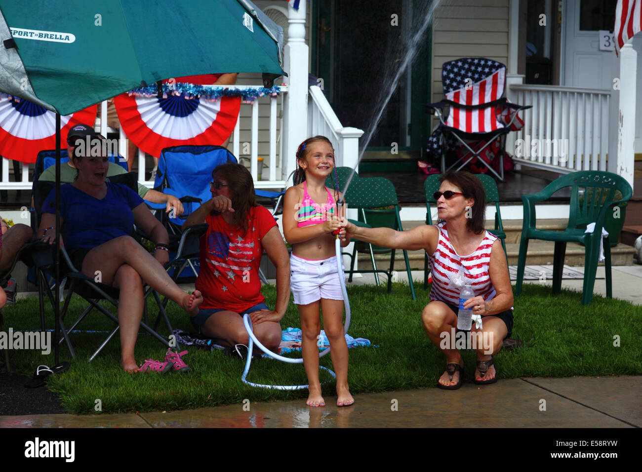 Ragazza e sua madre che giocano con hosepper di fronte al portico il 4th luglio festa pubblica Independence Day, Catonsville, Maryland, USA Foto Stock