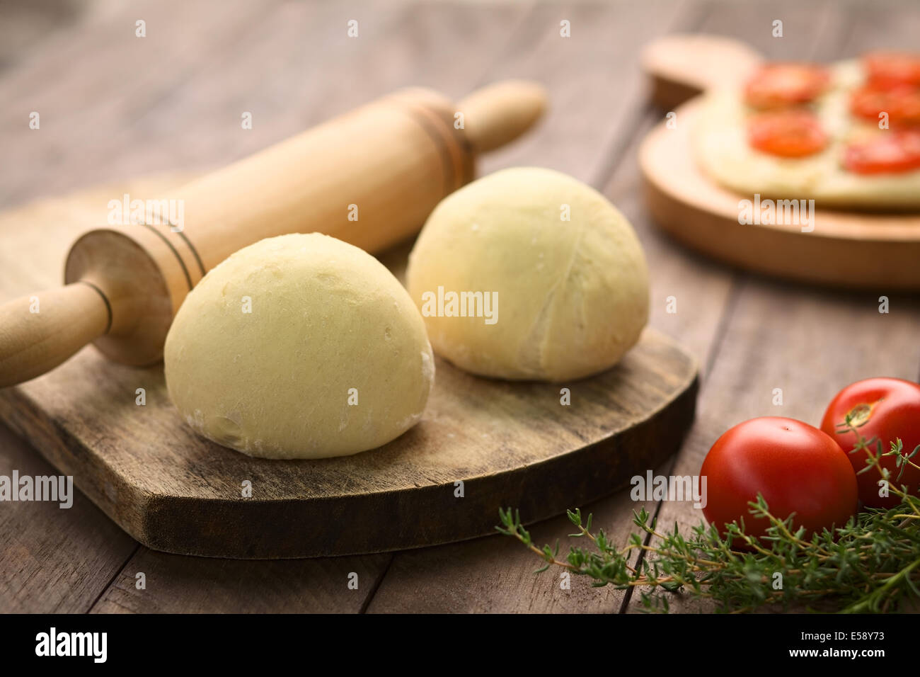 Palline di pasta lievitata per la pizza o la pasta con il mattarello sulla tavola di legno, i pomodori e il timo in parte anteriore Foto Stock