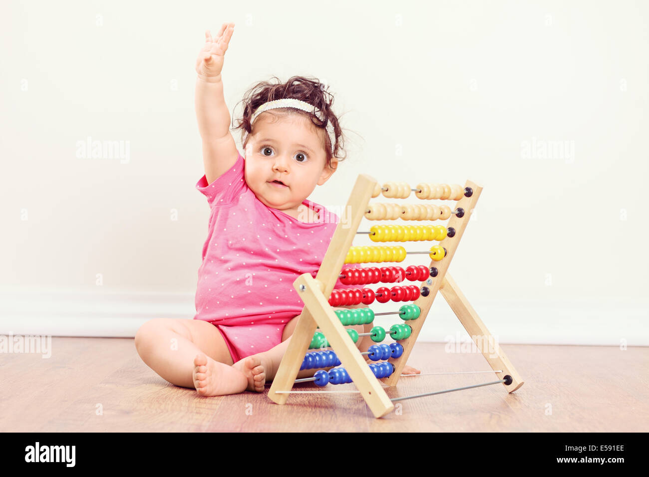 Baby ragazza seduta sul pavimento e alzando la mano con un abaco accanto a lei Foto Stock