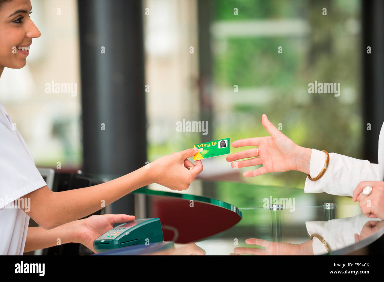 Donna di dare sicurezza sociale francese card al receptionist presso ospedale reception Foto Stock