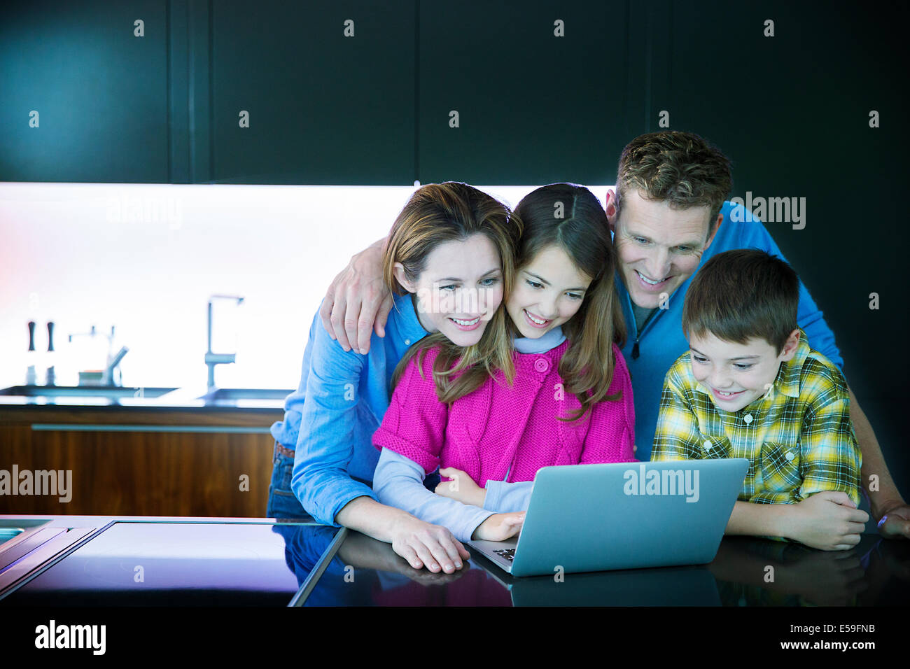 La famiglia tramite computer portatile in cucina Foto Stock