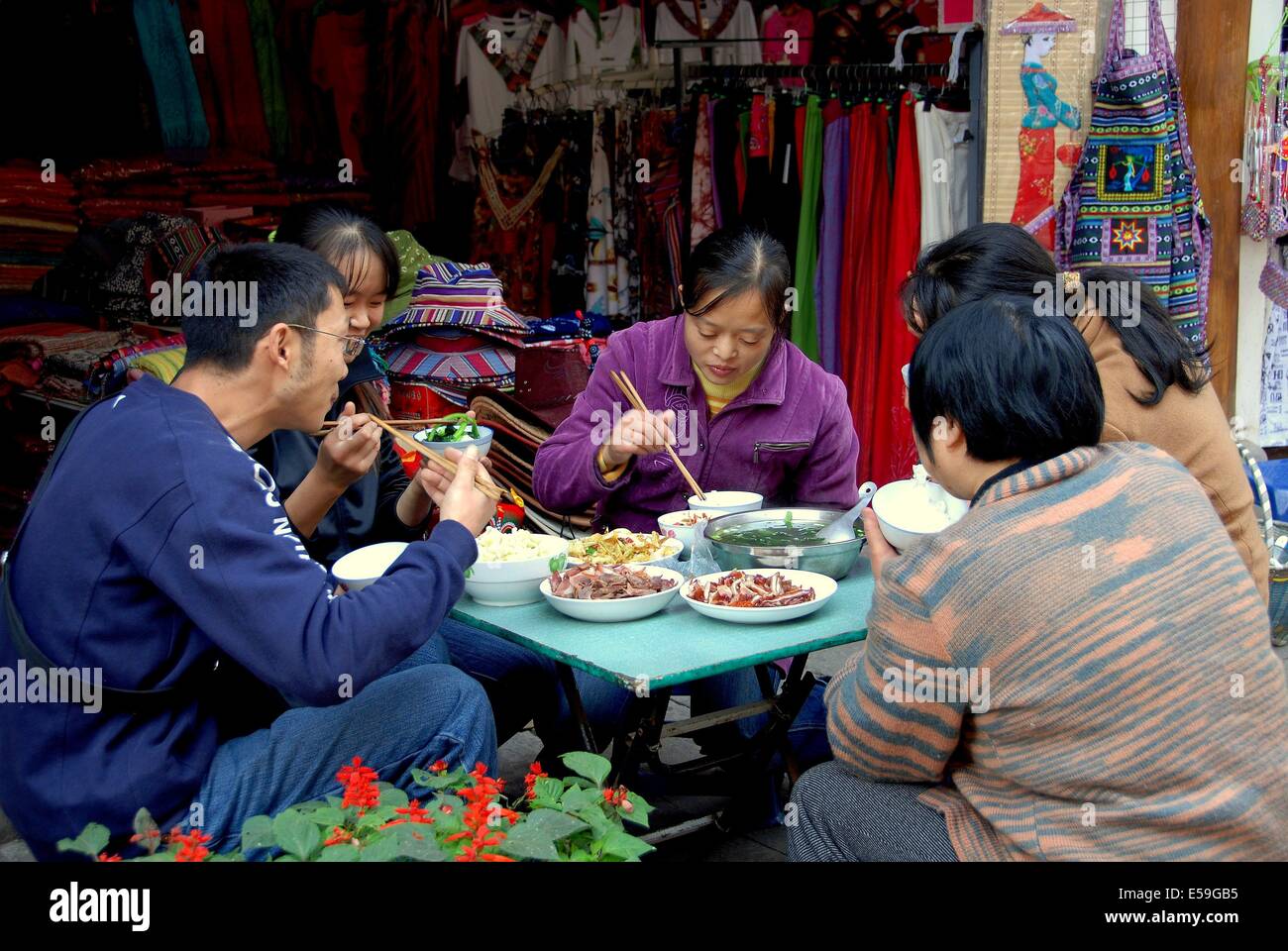 Huang Long Xi in Cina: i negozianti seduti ad un tavolo di fronte a loro abbigliamento e artigianato shop di mangiare il pranzo Foto Stock