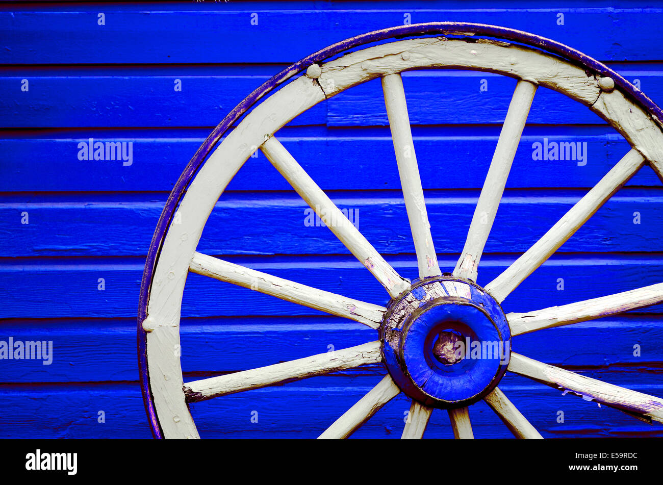 Vecchio weathered ruota di carro appoggiata contro blu dipinti a muro Foto Stock