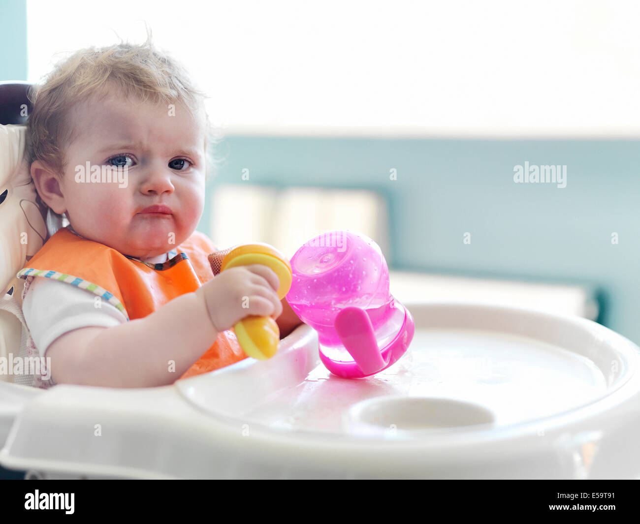 Bambina gioca con sippy cup in sedia alta Foto Stock