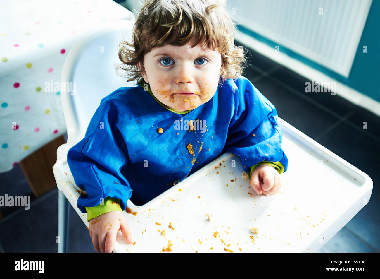 Confuso Baby girl eating in sedia alta Foto Stock
