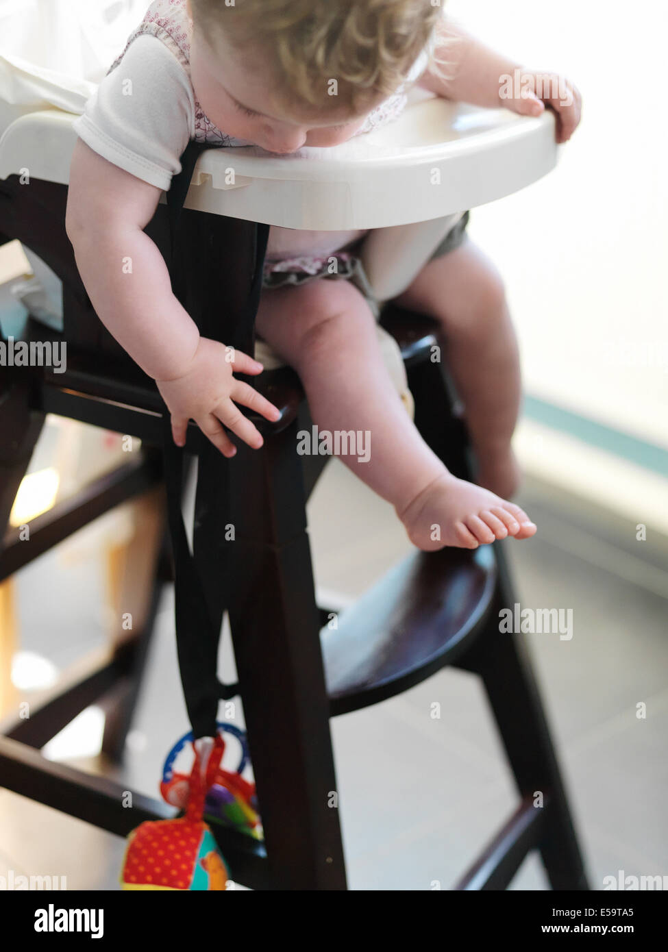 Baby girl in sedia alta per raggiungere il giocattolo Foto Stock