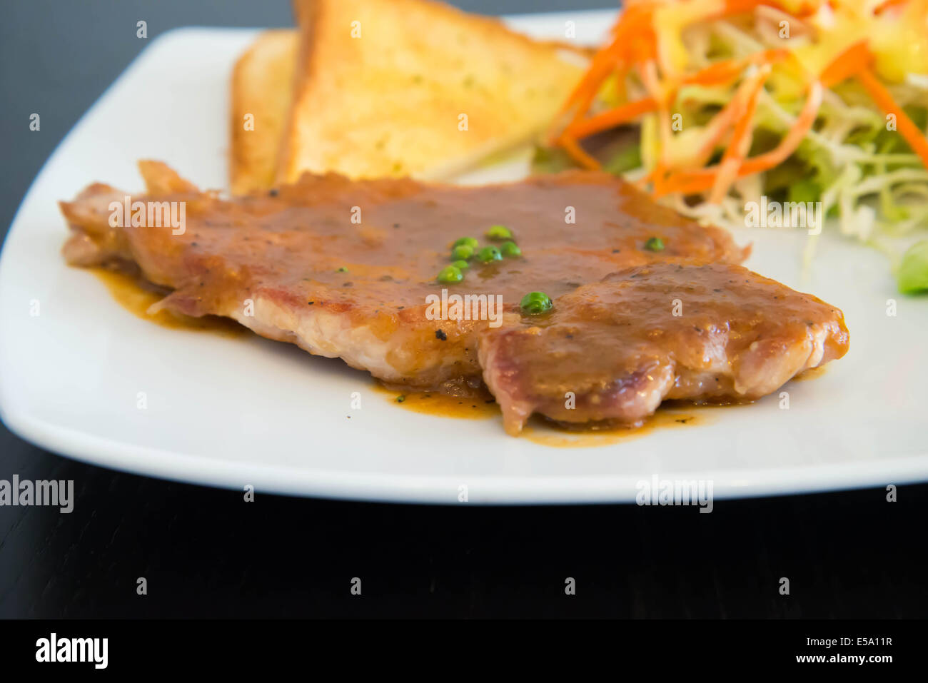 Bistecca di carne di maiale con pane tostato su un tavolo di legno. Foto Stock