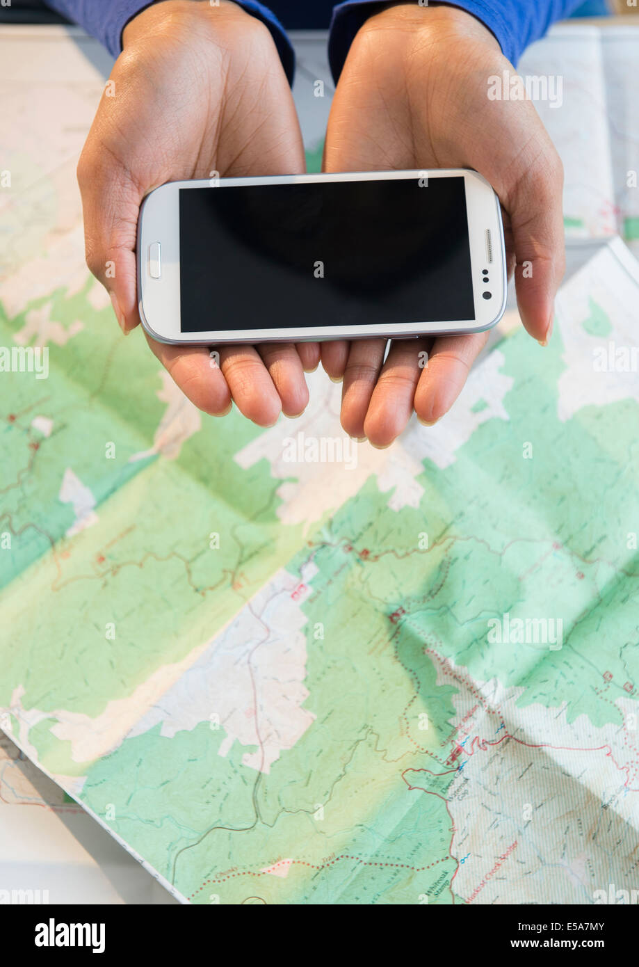 Razza mista donna azienda telefono cellulare su mappa Foto Stock