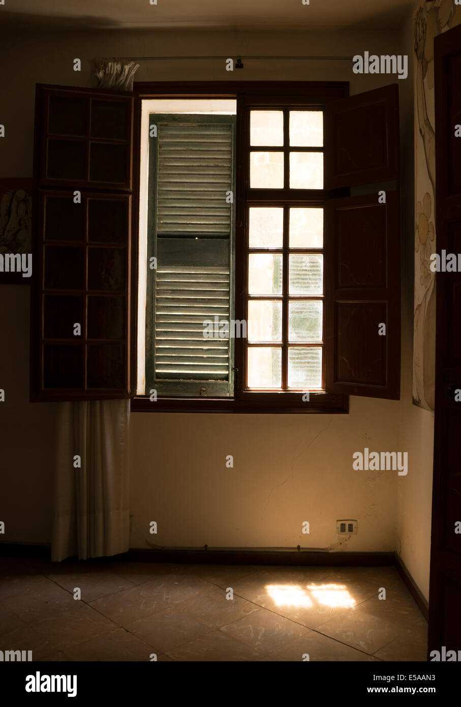 Vista da un interno (camera) di una finestra con persiane, tapparelle interno aperto, un otturatore esterno chiuso, pool di luce sul pavimento. Foto Stock