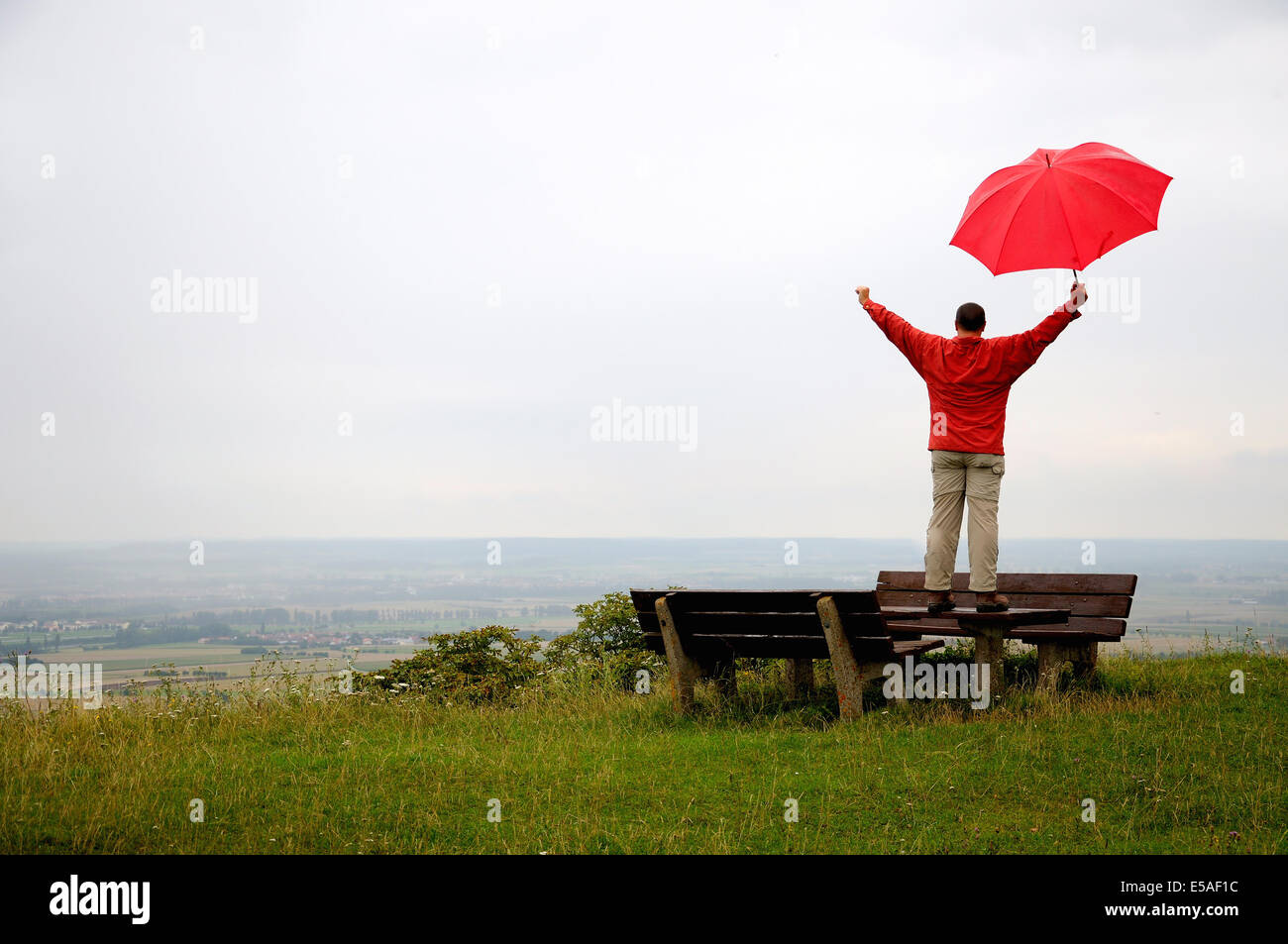 Uomo felice con il rosso ombrello in mano in piedi su un banco di lavoro in corrispondenza di un punto di vista Foto Stock