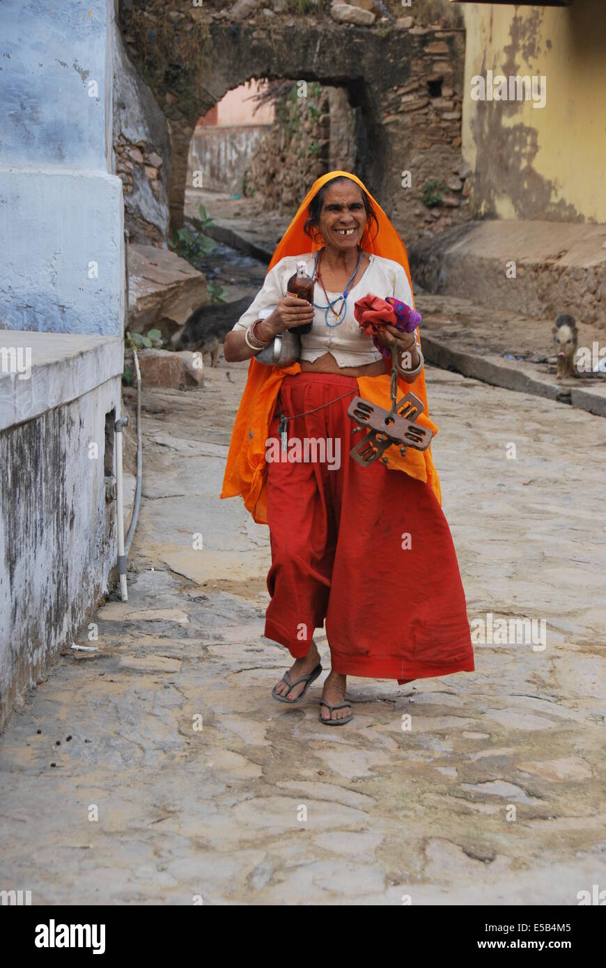 India. Il Rajasthan. Donna del villaggio. Vestito in arancione . medicina bottiglia. camminando in strada. Un grande sorriso. Foto Stock