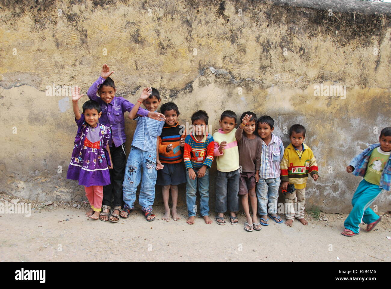 India. Il Rajasthan. I bambini del villaggio contro la parete ruvida.Una ragazza.nove ragazzi. gesticolando e sorridente. Foto Stock