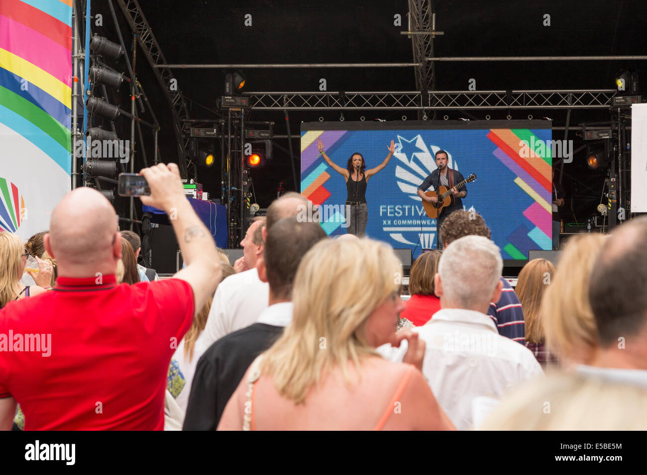 Un grande gruppo guarda un uomo e una donna eseguire sul palco e di canto e di eseguire sulla chitarra acustica, West End Festival, Glasgow, Scotland, Regno Unito, 2014 Foto Stock