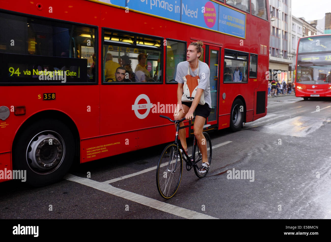 Ciclista e gli autobus di Londra in un giorno di pioggia Foto Stock