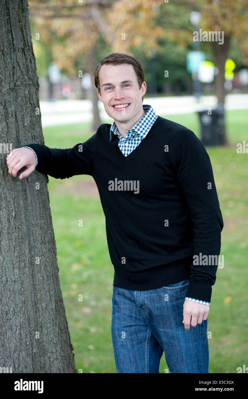 Un attraente giovane maschio modello in posa da un albero che indossa un maglione e un pulsante giù. Foto Stock