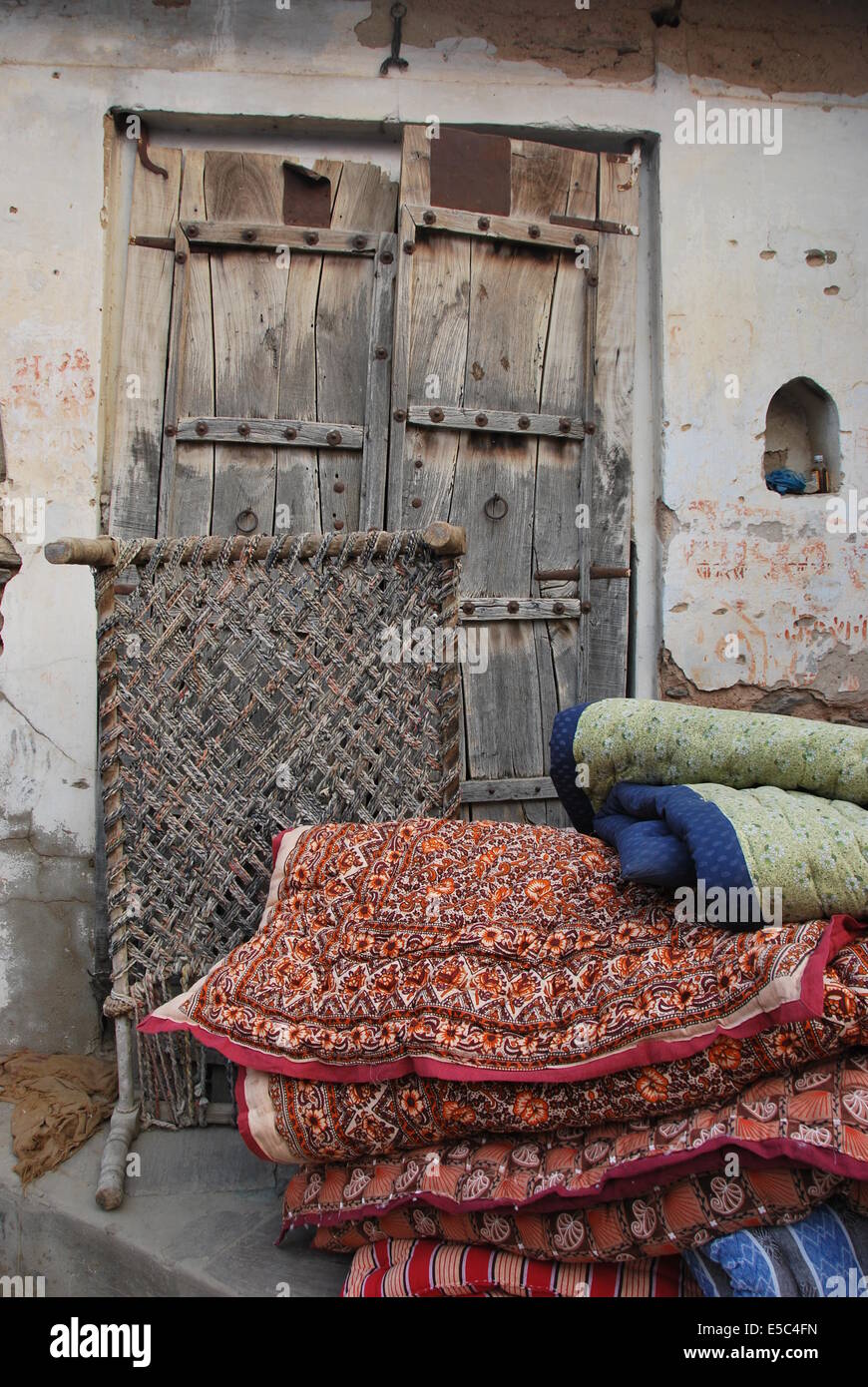 India. Il Rajasthan. La scena del villaggio. Porta in legno. Muro intonacato. Letto. Durries.tessili. Materiale modellato. Foto Stock