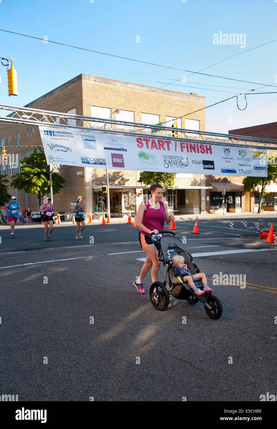 Donna in 5K o 10K marathon race crossing traguardo con il bambino nel passeggino Foto Stock