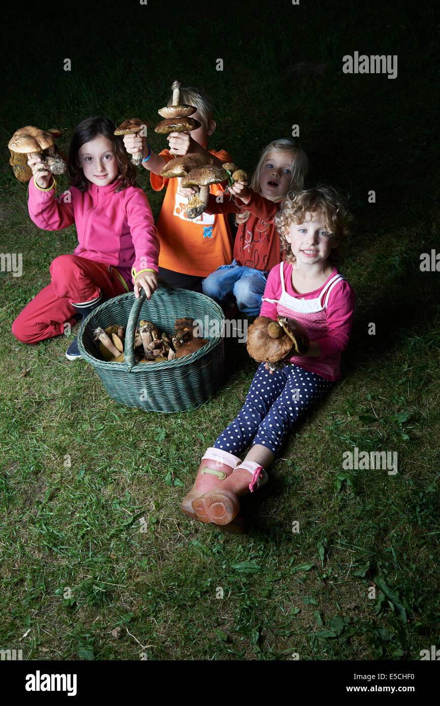 Gruppo di ragazzi e ragazze ragazzo seduto da cesto pieno di funghi su erba verde prato fuori Foto Stock