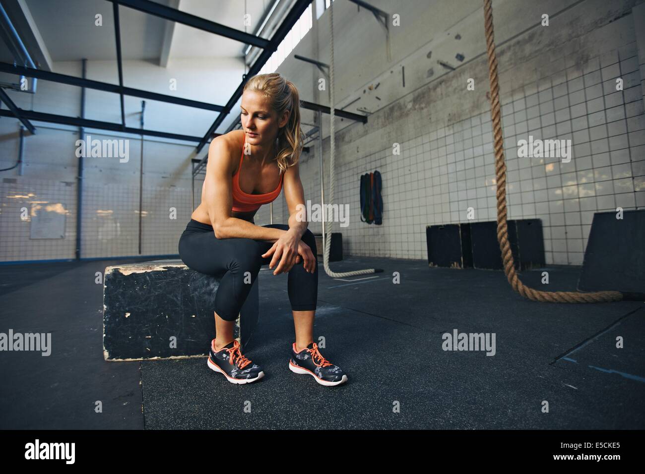 Caucasian atleta donna seduta su una casella nella palestra di pensare. Montare la giovane donna prendendo pausa dopo il suo allenamento in palestra. Foto Stock