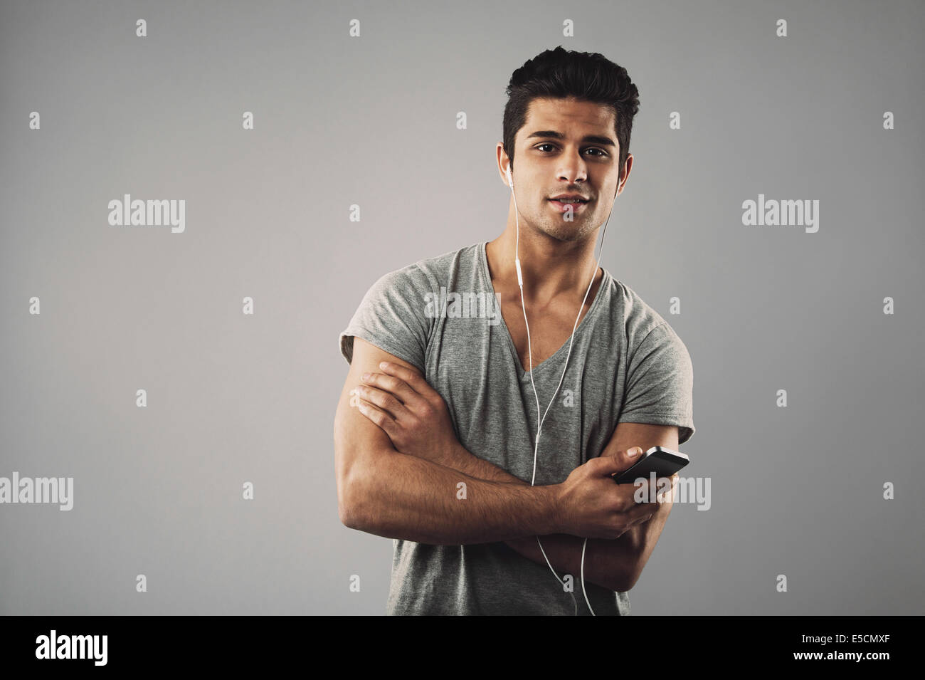 Casual giovane uomo che ascolta la musica sul telefono cellulare. Ispanico modello maschile che indossa gli auricolari e ascoltare musica tramite il suo telefono. Foto Stock