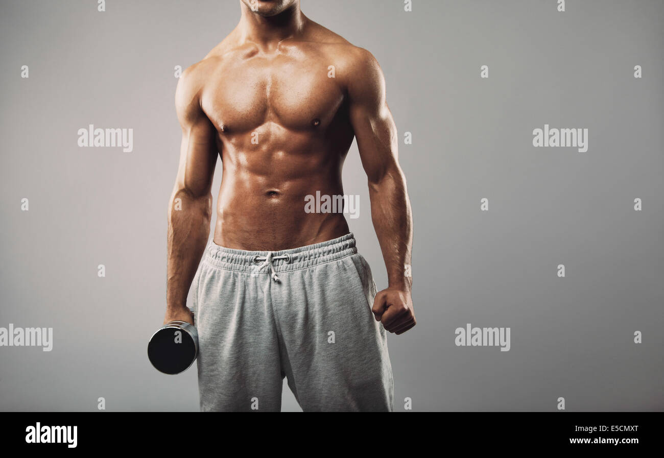 Immagine ritagliata del giovane maschio muscolare modello fitness indossando tute Tenendo un manubrio contro uno sfondo grigio. Montare il giovane uomo Foto Stock
