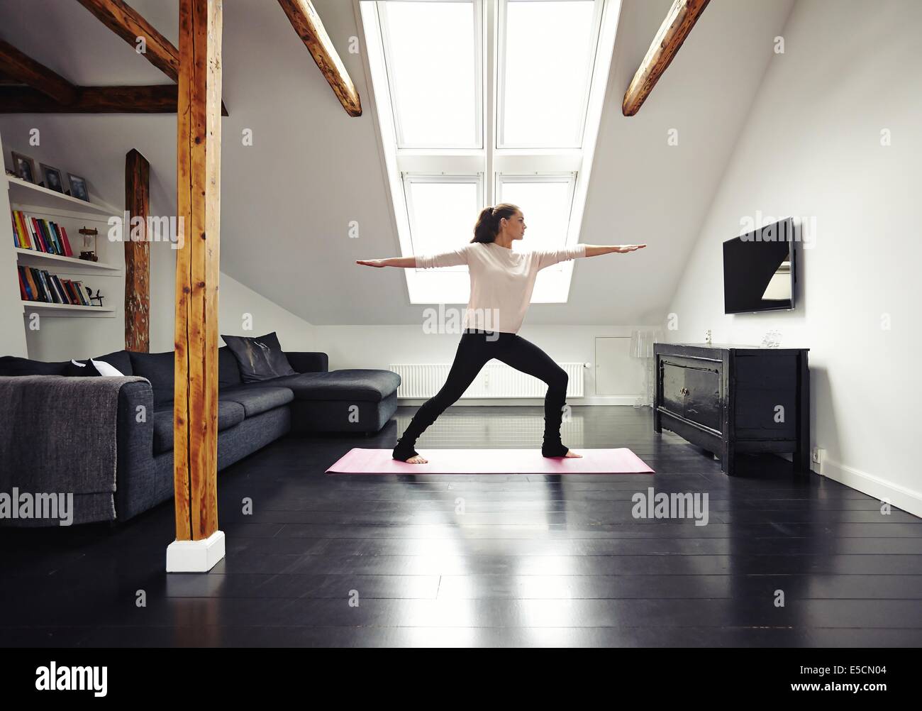 Lunghezza completa immagine di montare la donna in piedi sul tappeto di esercizio con le braccia aperte facendo yoga in camera amorevole. Caucasian modello femminile Foto Stock