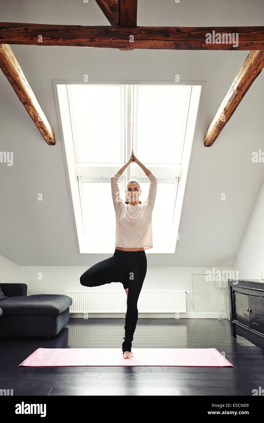 Giovane donna a praticare yoga in salotto. Sani di sesso femminile in piedi su una gamba sola e la meditazione a casa. Montare femmina in posa ad albero d Foto Stock