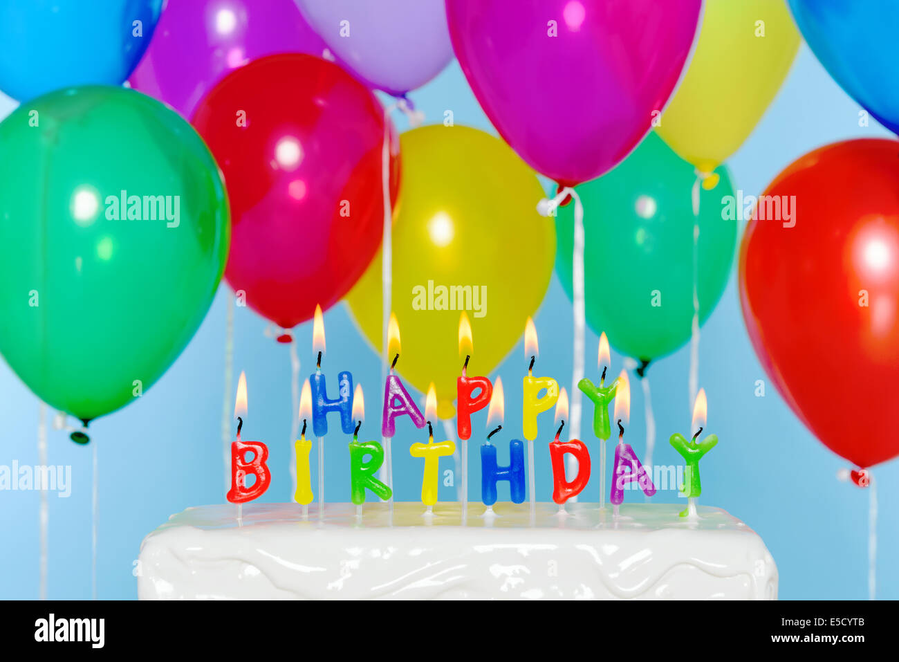 Buon compleanno candela lettere su una torta con palloncini colorati in background. Foto Stock