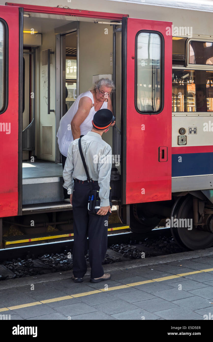 Anziani passeggero femmina chiedendo informazioni al dipendente ferroviario / ticket inspector da treno su piattaforma in stazione ferroviaria Foto Stock