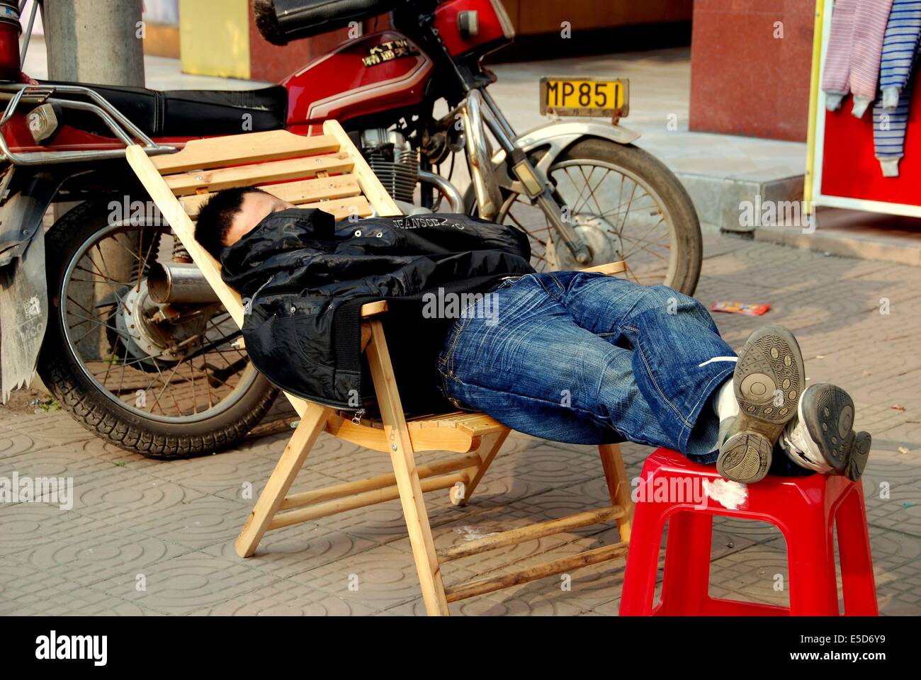 Il jiu CHI TOWN, CINA: uomo prendendo un pisolino fuori in un pomeriggio soleggiato di fronte a un negozio di abbigliamento Foto Stock