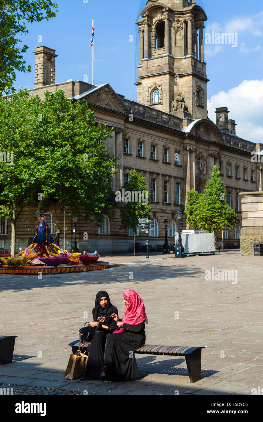 Due giovani ragazze musulmane in abito tradizionale seduti di fronte al Municipio, la piazza del mercato, Preston, Lancashire, Regno Unito Foto Stock