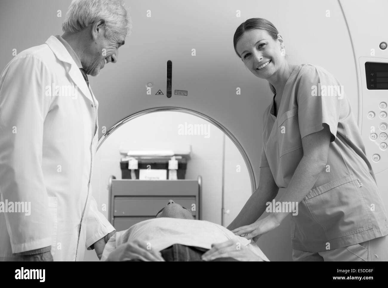 Uomo in 40s sottoposta a MRI scan aperto, maschio e femmina medico sorridendo a lui. Foto Stock