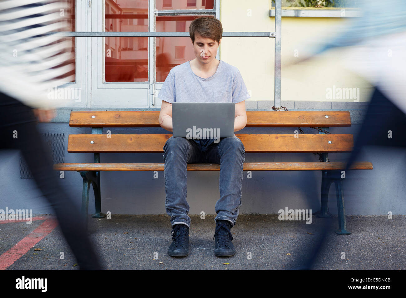 Uomo seduto su un banco di lavoro con computer portatile con persone di passaggio Foto Stock